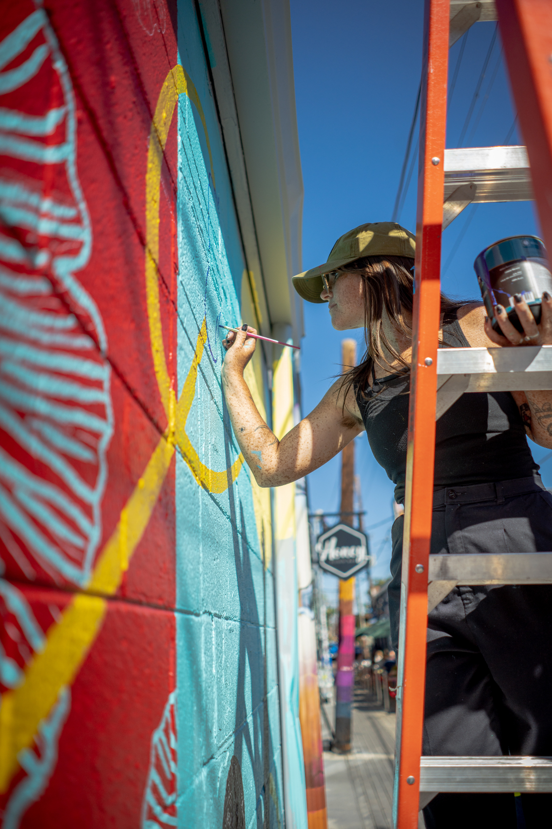 Mural artist Valerie Rose stands on a ladder and paints details onto the mural. 