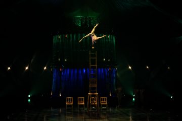 Person balancing on chairs on stage